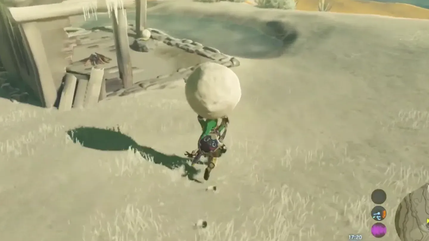 Link carrying a snowball past wooden ruins on the snowy summit