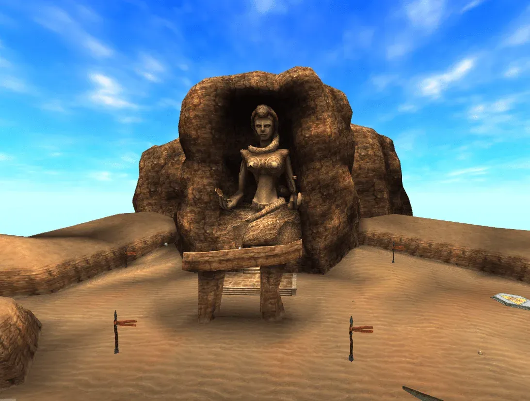 The Desert Colossus under a blue sky: a giant stone statue of a seated woman carved into the rock, with sand all around