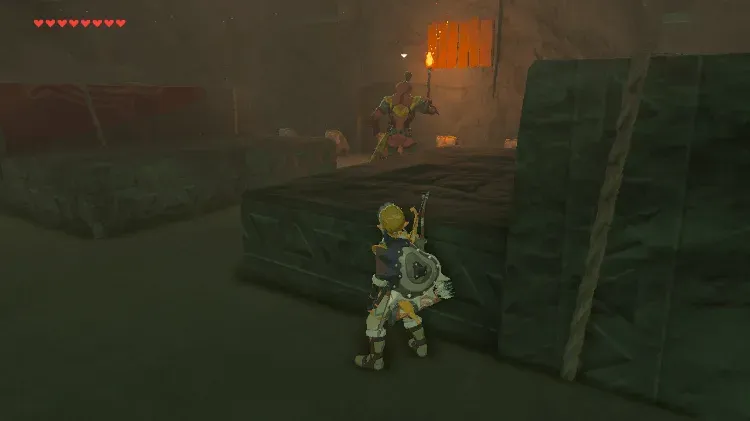 Link crouching behind a stone block while a Yiga Blademaster stands guard by a door in the hideout