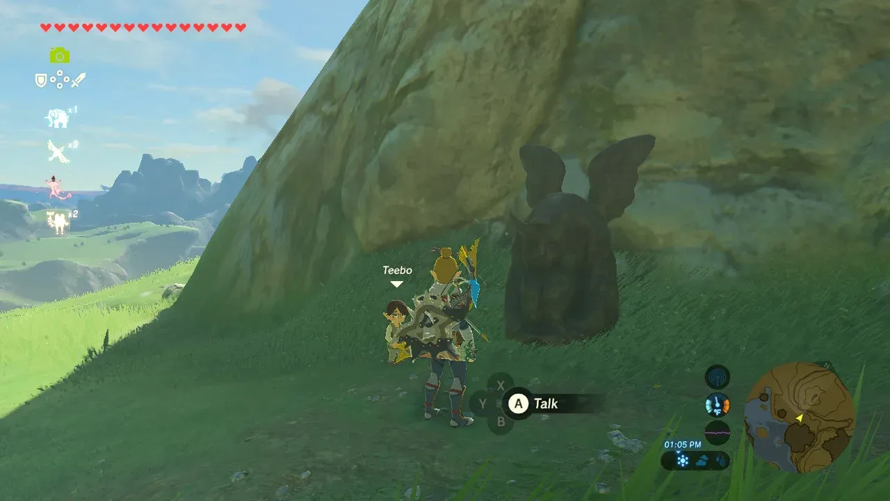 Link next to Teebo in front of the Horned Statue under a rock face in Hateno Village