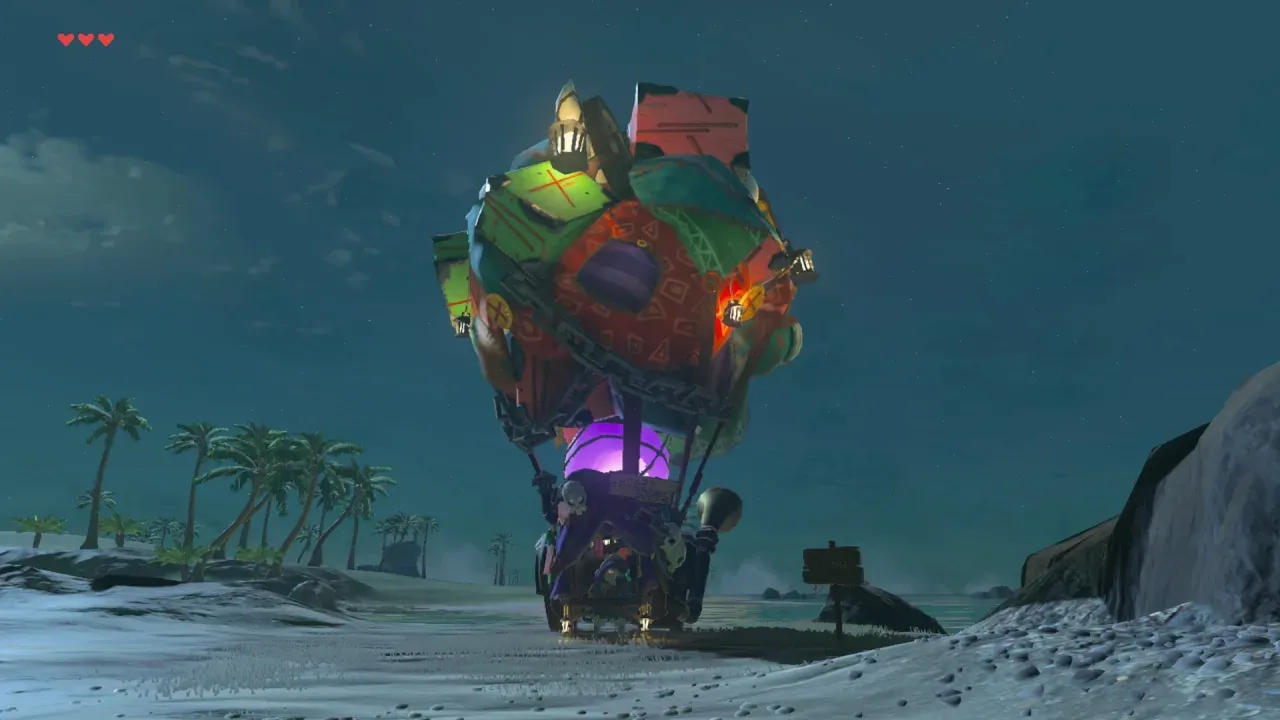 At night, a big cart covered in monster decorations stands on a beach beside a wooden sign
