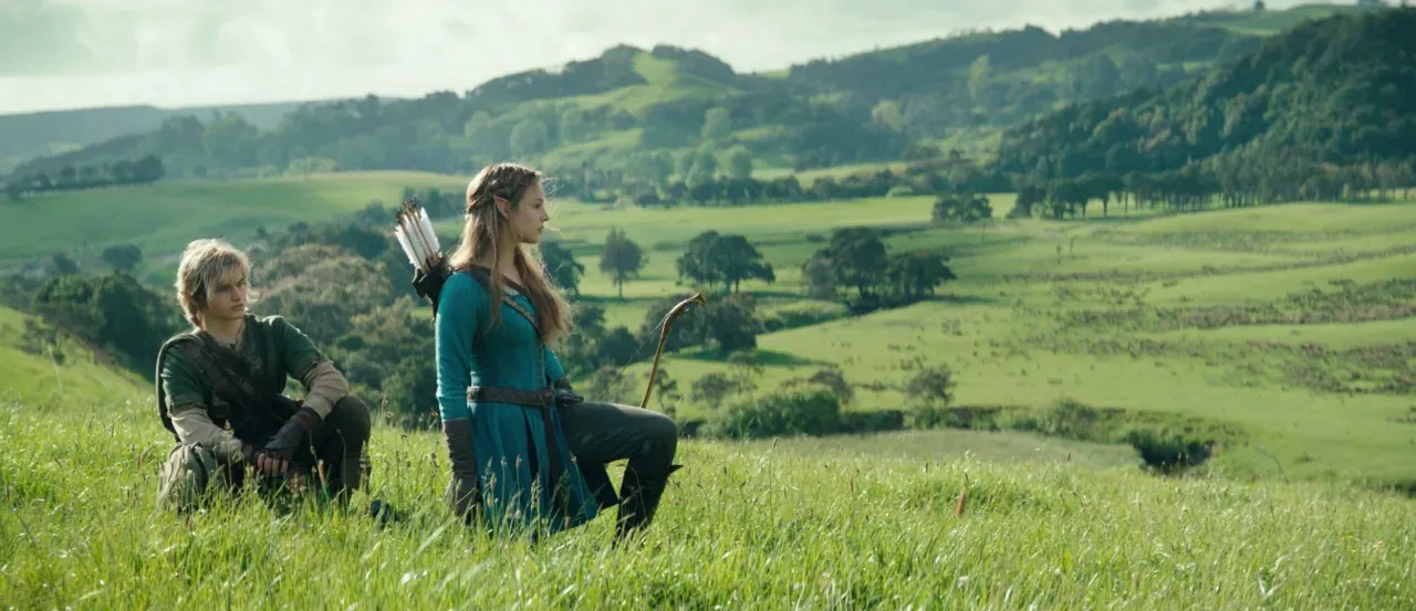 Link and Zelda in costume, kneeling in tall grass on a green hillside