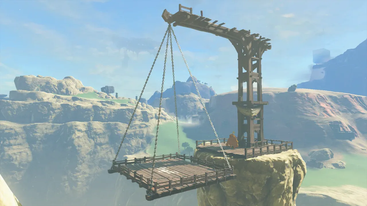 A wooden platform hanging on chains from a tall frame at the edge of a cliff
